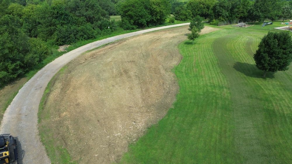 Aerial view of a cleared area beside a winding path with green grass and scattered trees.
