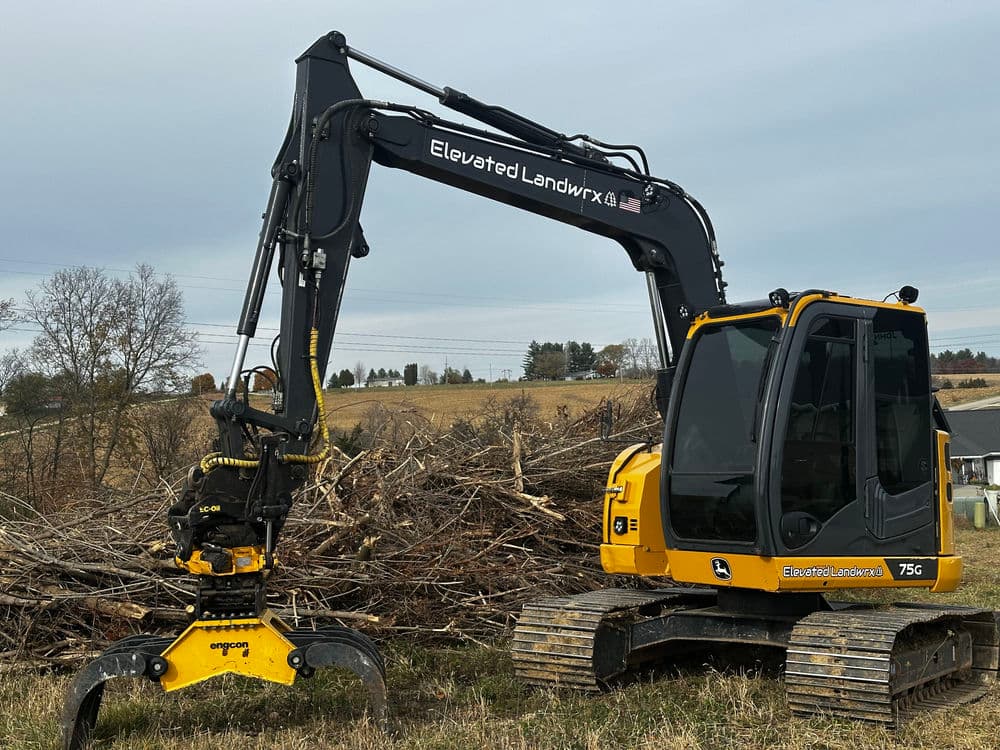Heavy-duty excavator with grapple attachment clearing timber in rural area.