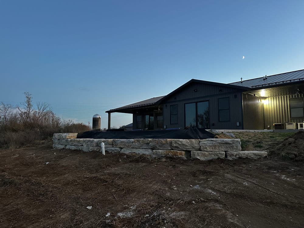 Modern farmhouse with stone foundation at dusk, featuring a sleek design and surrounding landscape.