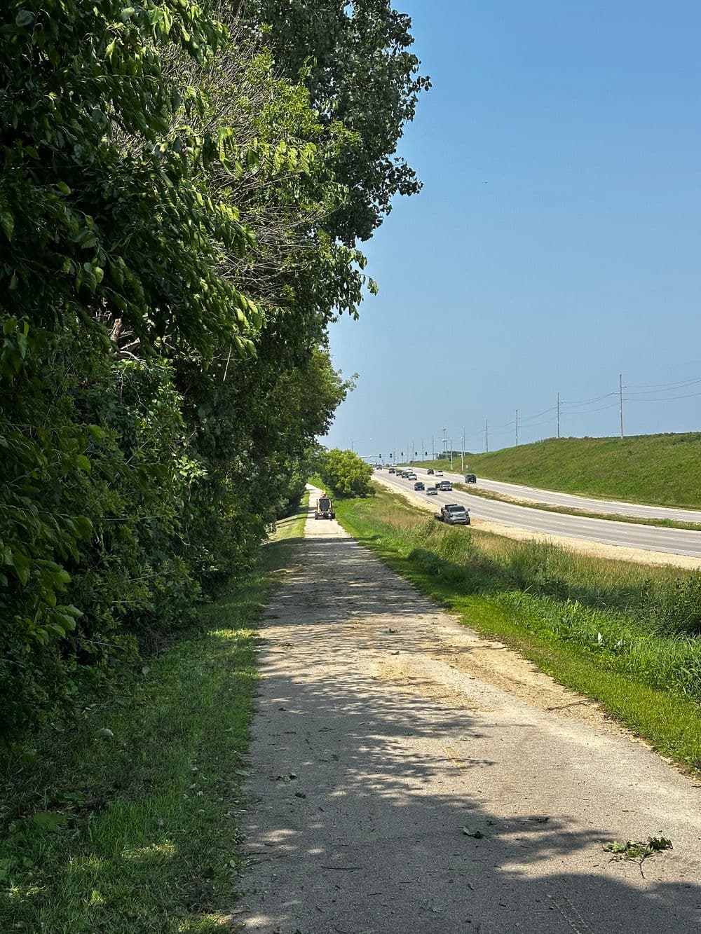 Bike path alongside a highway surrounded by greenery under a clear blue sky.