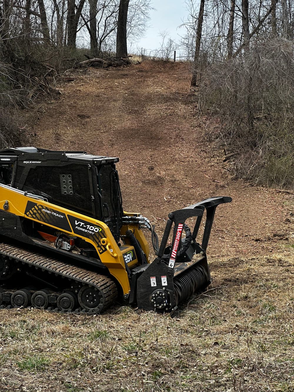 Skid steer loader with mulching head clearing land in wooded area.