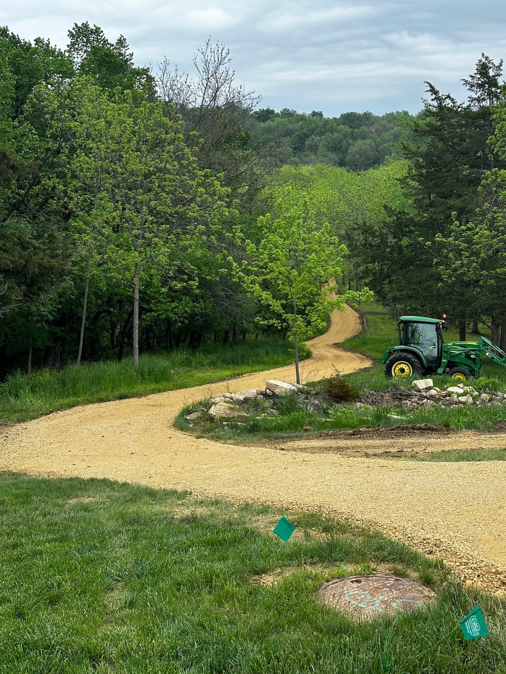Gravel path lined with trees, leading to a green tractor in a serene landscape.