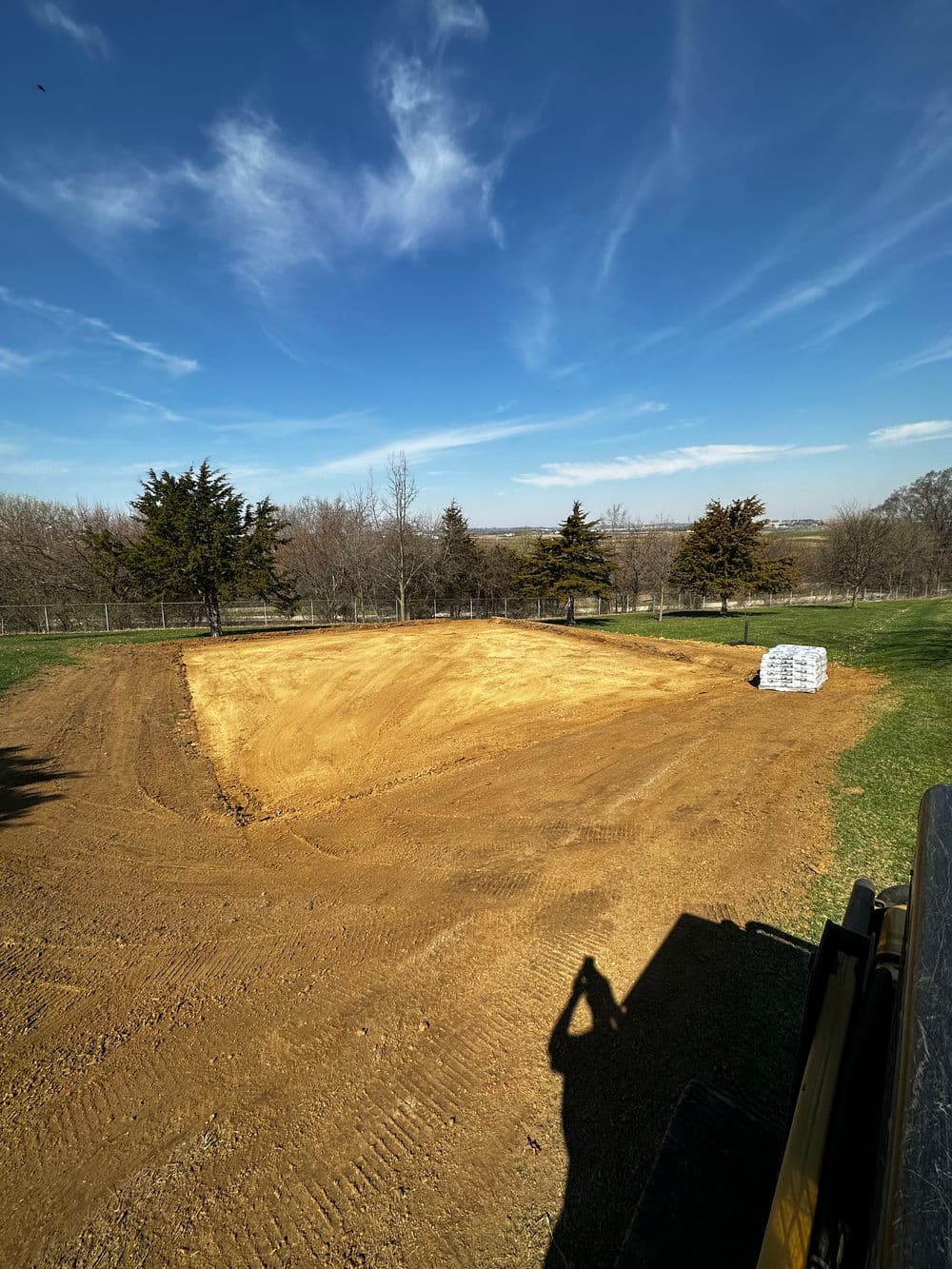 Cleared land preparation with dirt for construction under a blue sky and trees.